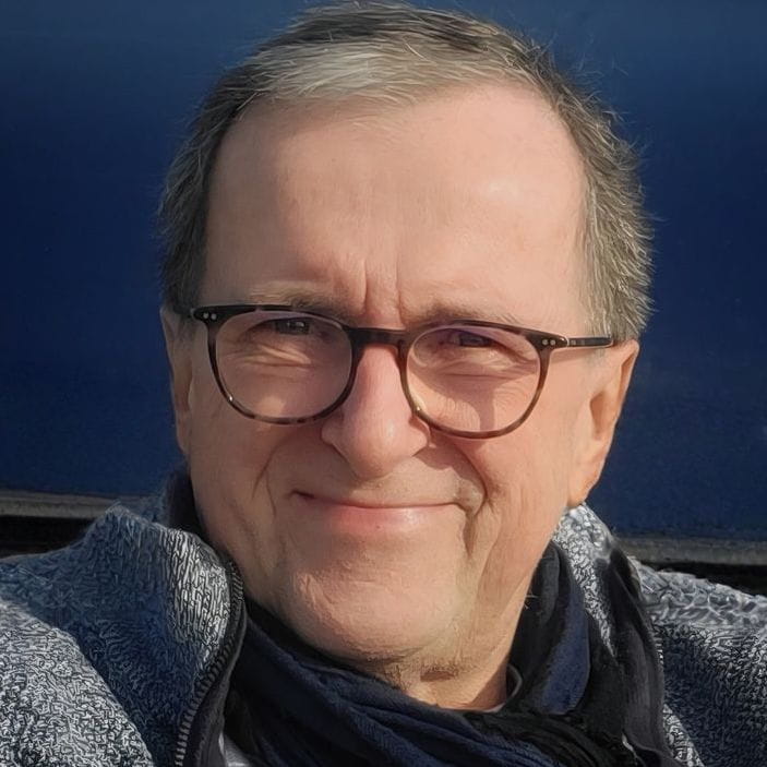 Porträt von Godehart mit Brille, hellblauem Hemd und dunkelblauem Hintergrund