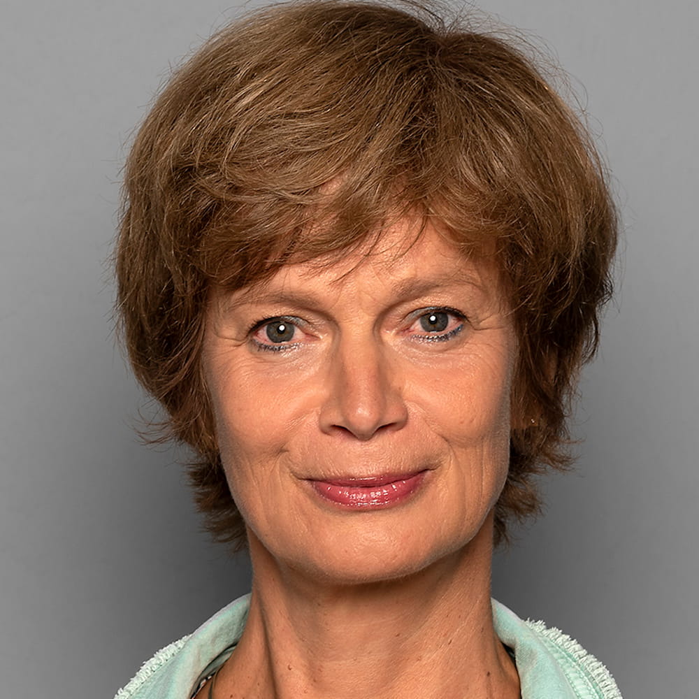Porträt von J Lorenz mit braunem Haar und rosarotem Lippenstift vor grauem Hintergrund