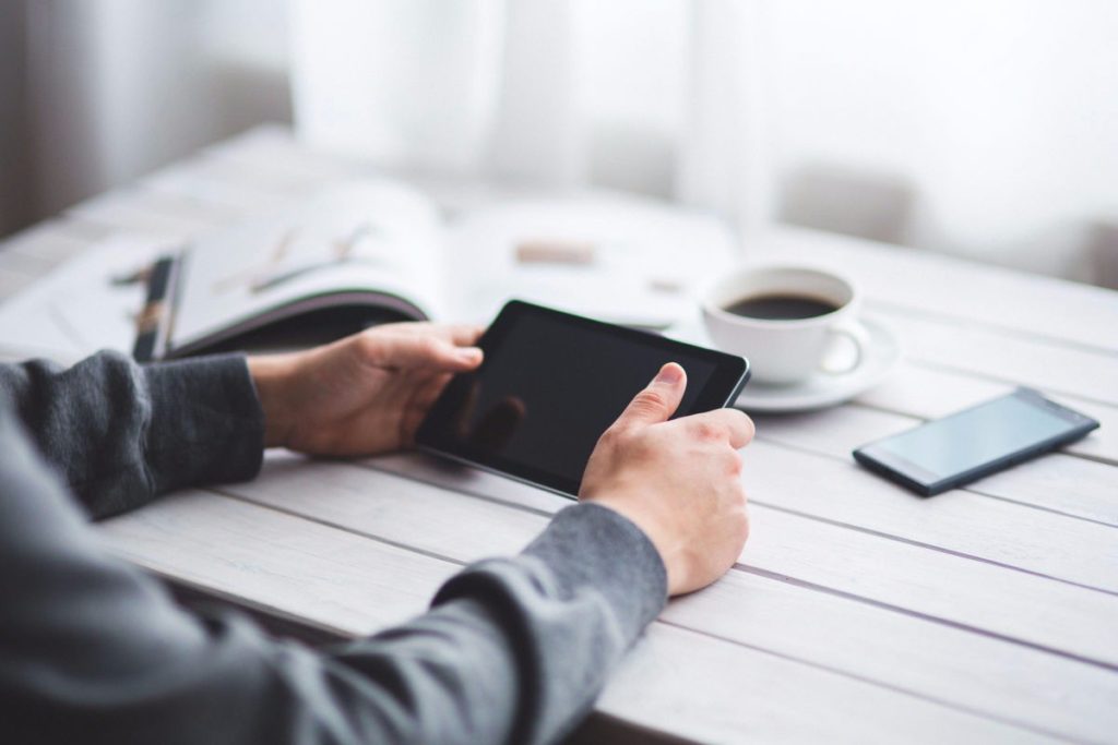 Jahres-Flatrate für die ET-Akademie 2 Person hält Tablet in Händen am Schreibtisch mit Buch, Kaffee und Smartphone