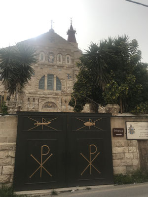 Schwarzes Tor mit Chi-Rho-Symbol und Kirche mit Kreuzen im Hintergrund