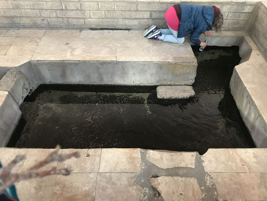 Person kniet an Taufstelle mit schwarzem Wasser im Becken