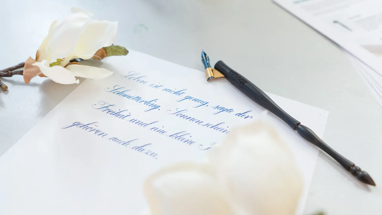 Kalligrafie-Handschrift auf Papier mit Feder und Tintenfass umgeben von Blüten