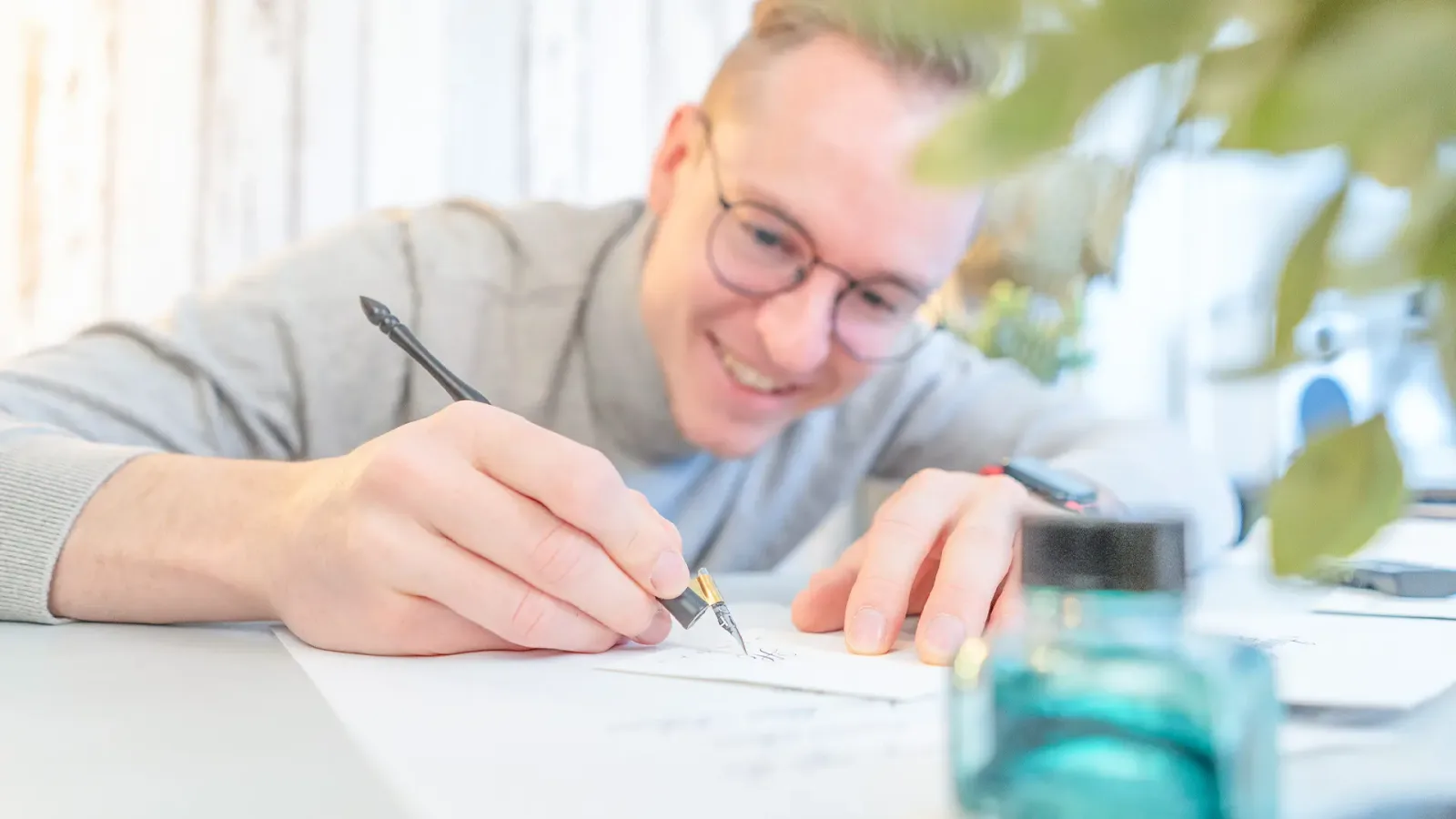 Kind mit Brille schreibt konzentriert mit Kalligrafie-Feder auf Papier umgeben von Blüten