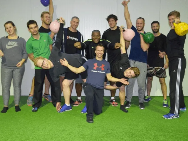 Gruppenfoto von Fitness-Kursteilnehmern mit bunten Kettlebells in Sporthalle