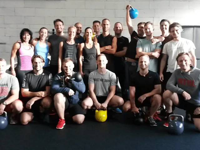 Fitness-Kursgruppe mit Kettlebells vor weißer Ziegelmauer