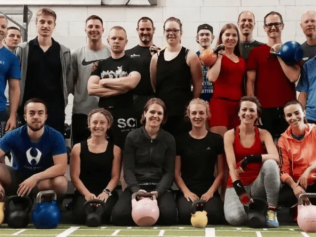Fitness-Kurs mit Teilnehmern, die bunte Kettlebells in verschiedenen Posen halten