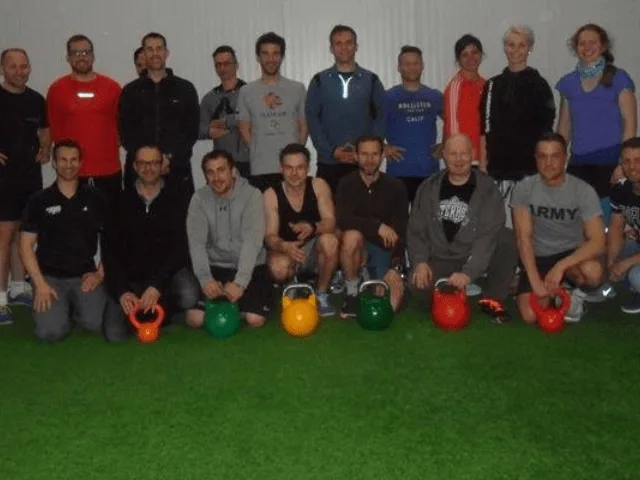 Große Trainingsgruppe mit bunten Kettlebells in Fitnesshalle