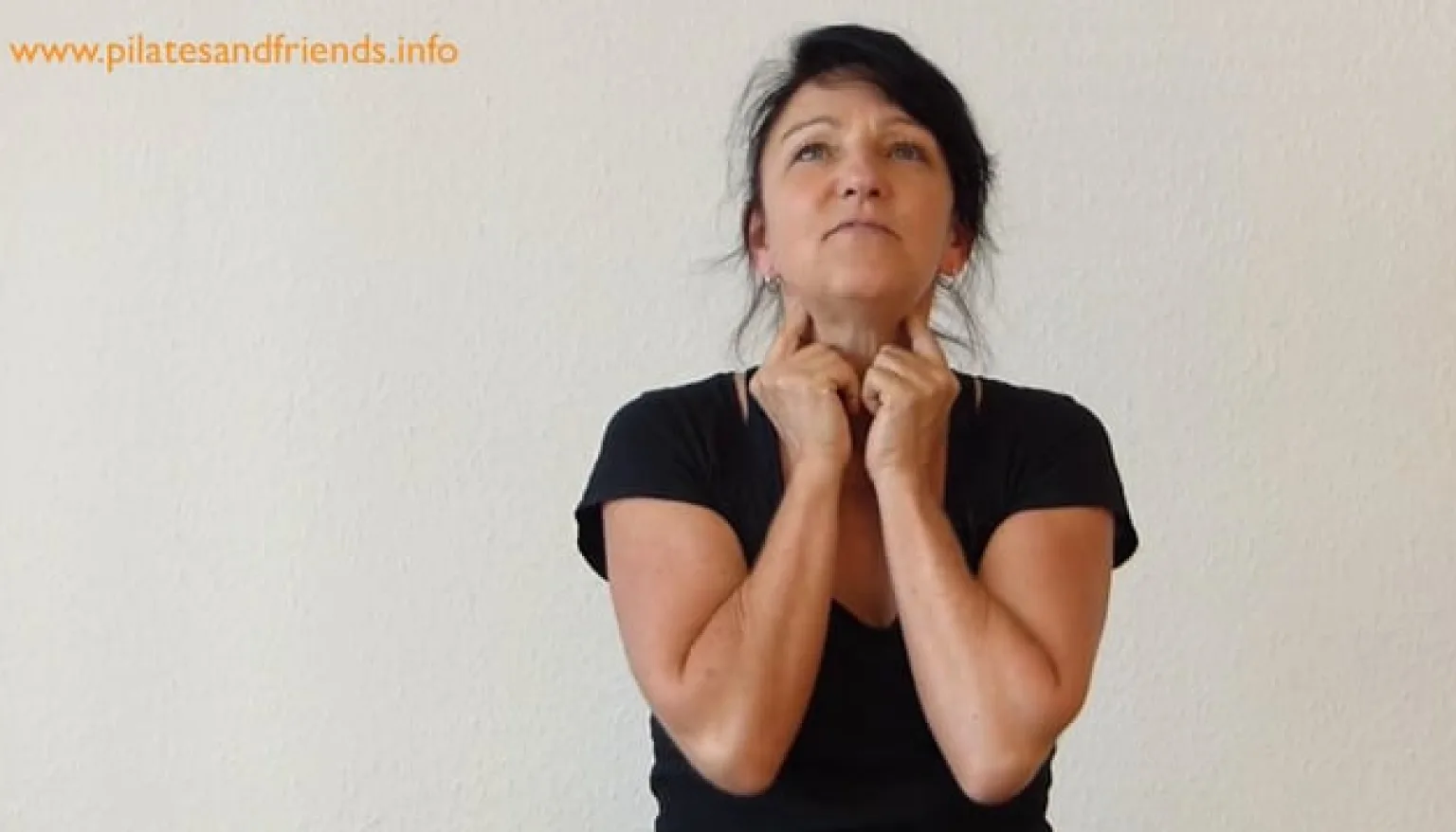 Kiefergelenk und Becken – Pilates-Videoworkshop von Claudia Lau 10 Frau in schwarzem T-Shirt führt Kiefergelenk-Entspannungsübung durch mit beiden Händen am Kinn