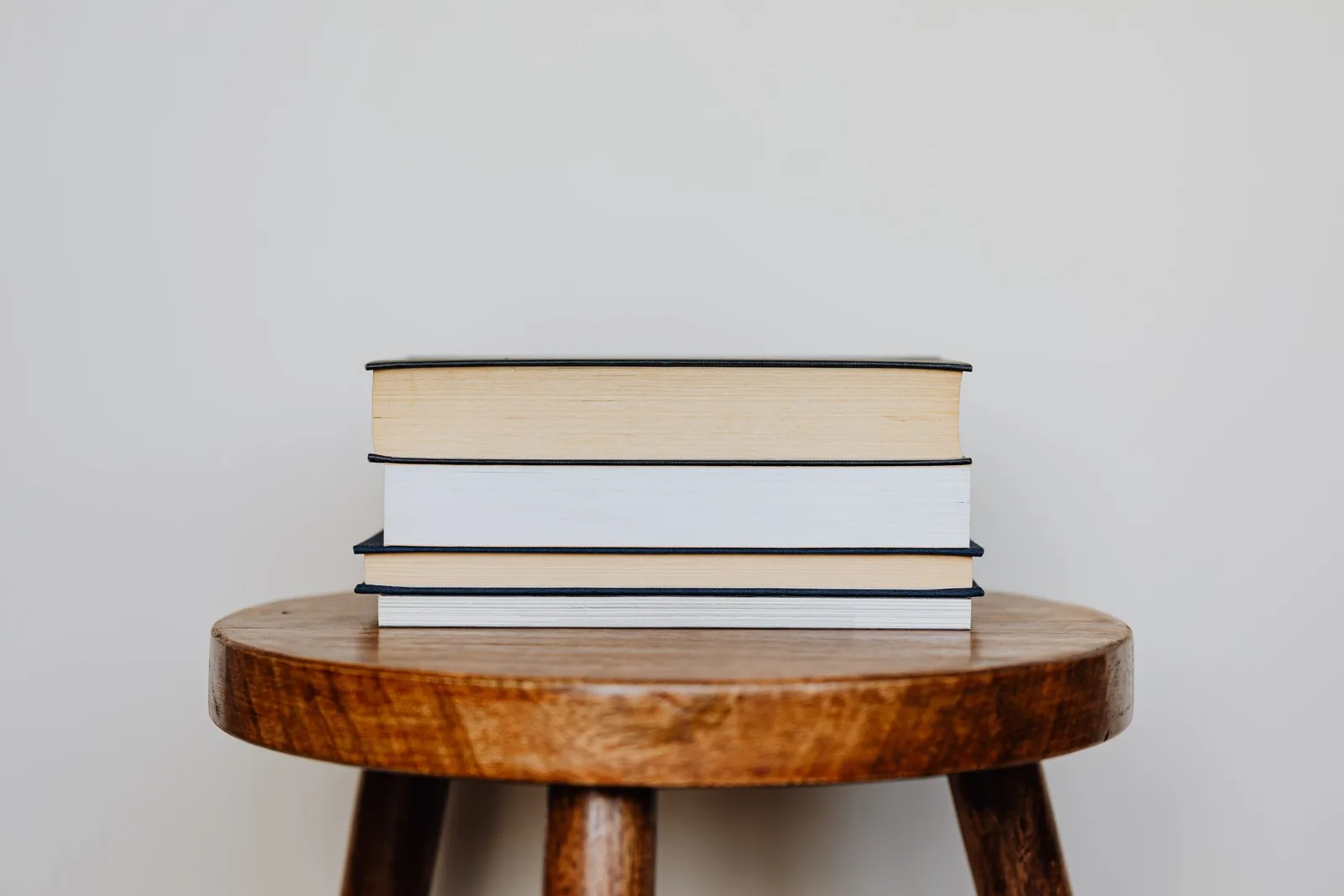 Stapel mit Büchern unterschiedlicher Farben auf rundem Holztisch vor grauem Hintergrund