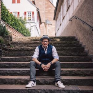 Matthias Zeitler, Mann mit Hut auf Steinstufen sitzend