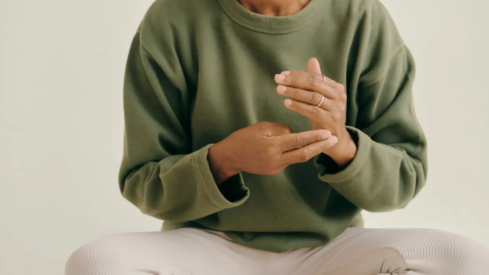 Klopf dich in deine Mitte: EFT – Videokurs zur Stressregulation 6 Person in grünem Sweatshirt führt EFT Klopftechnik mit beiden Händen auf Brust durch, sitzt vor hellem Hintergrund