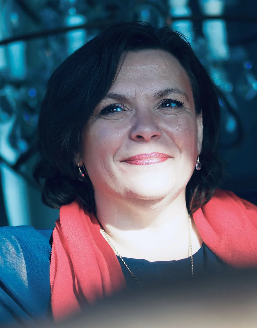 Christine Hofmann Portrait mit rotem Blazer vor blauem verschwommenem Hintergrund, direkter Blick, professionell