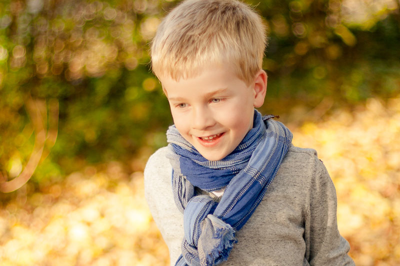 Fröhliches Kind in grauem Pullover und blauem Schal vor unscharfem herbstlichem Hintergrund