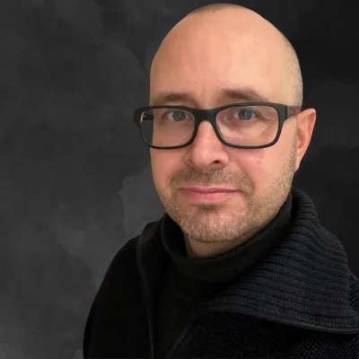 Kongresspaket Entdeckerin: Abzocke – Kurs zu spiritueller Abzocke 17 Porträt von Johannes Heim, Mann mit Brille und schwarzem Rollkragen vor grauem Hintergrund