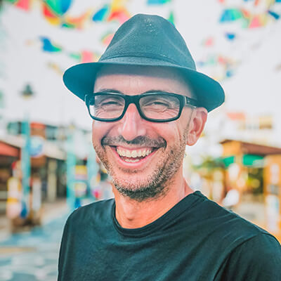 Mann mit Brille und blauem Hut vor buntem Graffiti-Hintergrund, lächelnd