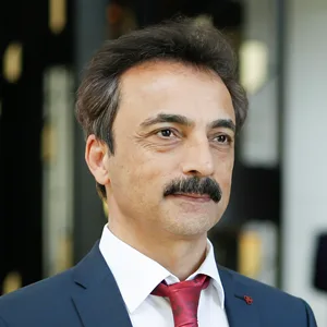 Kongresspaket Integrative Krebsmedizin – Teil 2 14 Porträt Dr. med. Hüseyin Sahinbas, Mann mit Schnurrbart im dunkelblauen Anzug