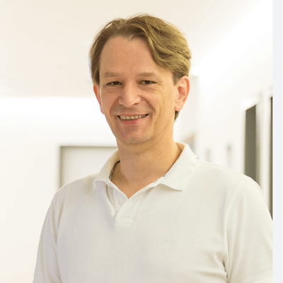 Kongresspaket – Interviews zu Geld-Bewusstsein 6 Dr. Bodo Schiffmann, Mann mit braunem Haar, weißem Poloshirt, lächelnd vor hellem Hintergrund