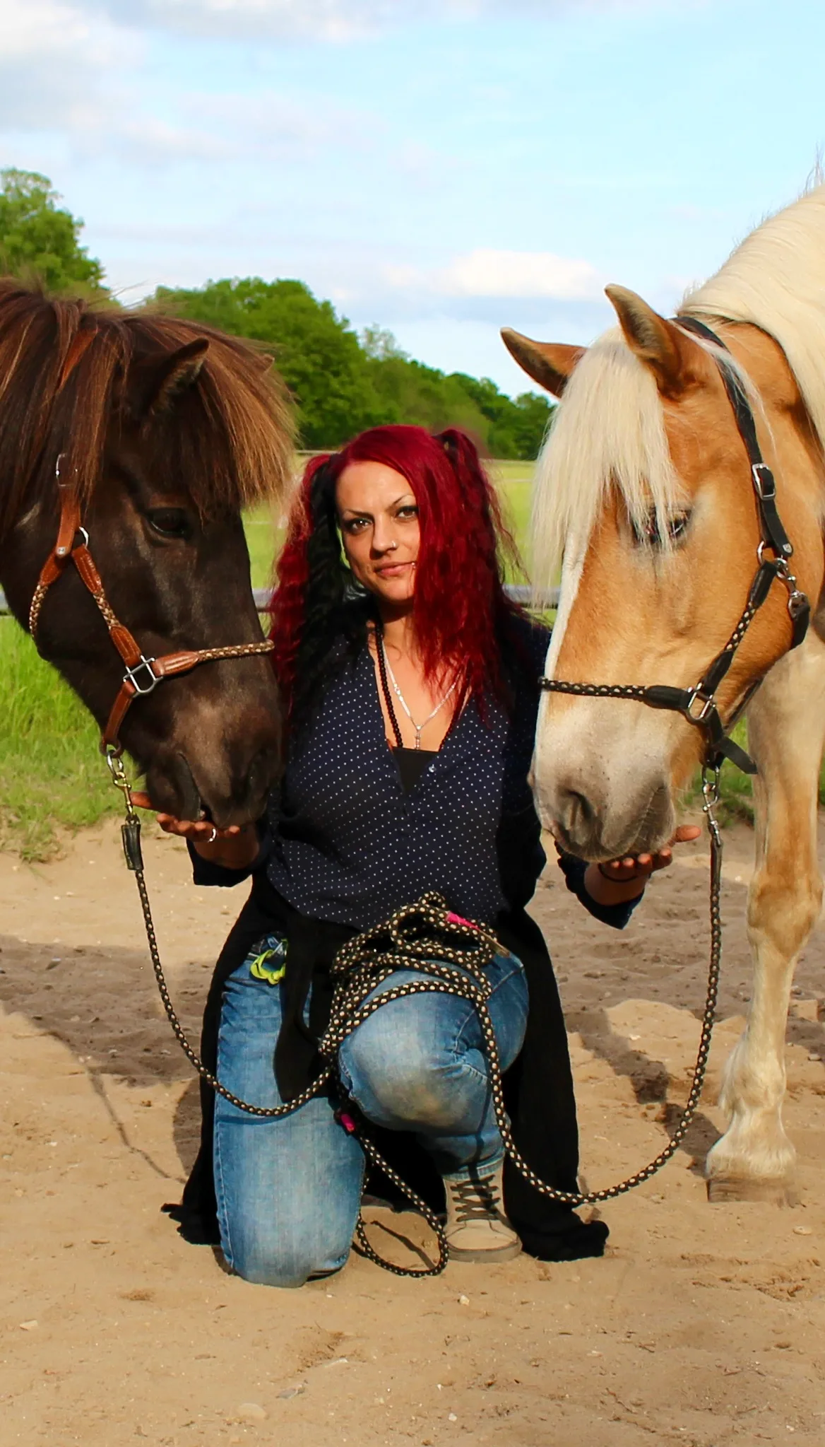 Yve Ehler mit roten Haaren zwischen zwei Pferden, dunkle Bluse und Jeans