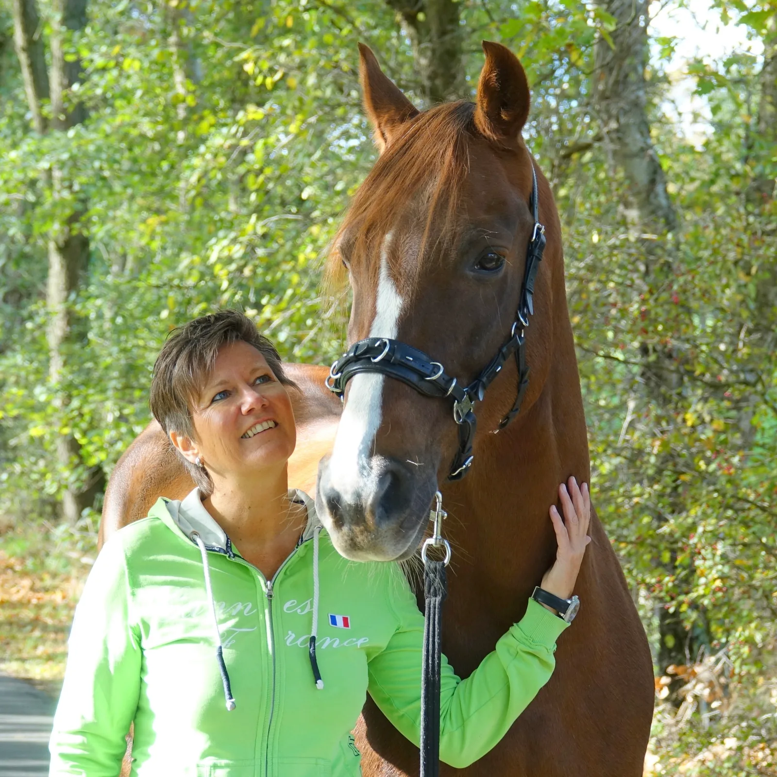 Angelika Hutmacher in grüner Jacke mit Pferd im Wald, Nahaufnahme Pferdegesicht
