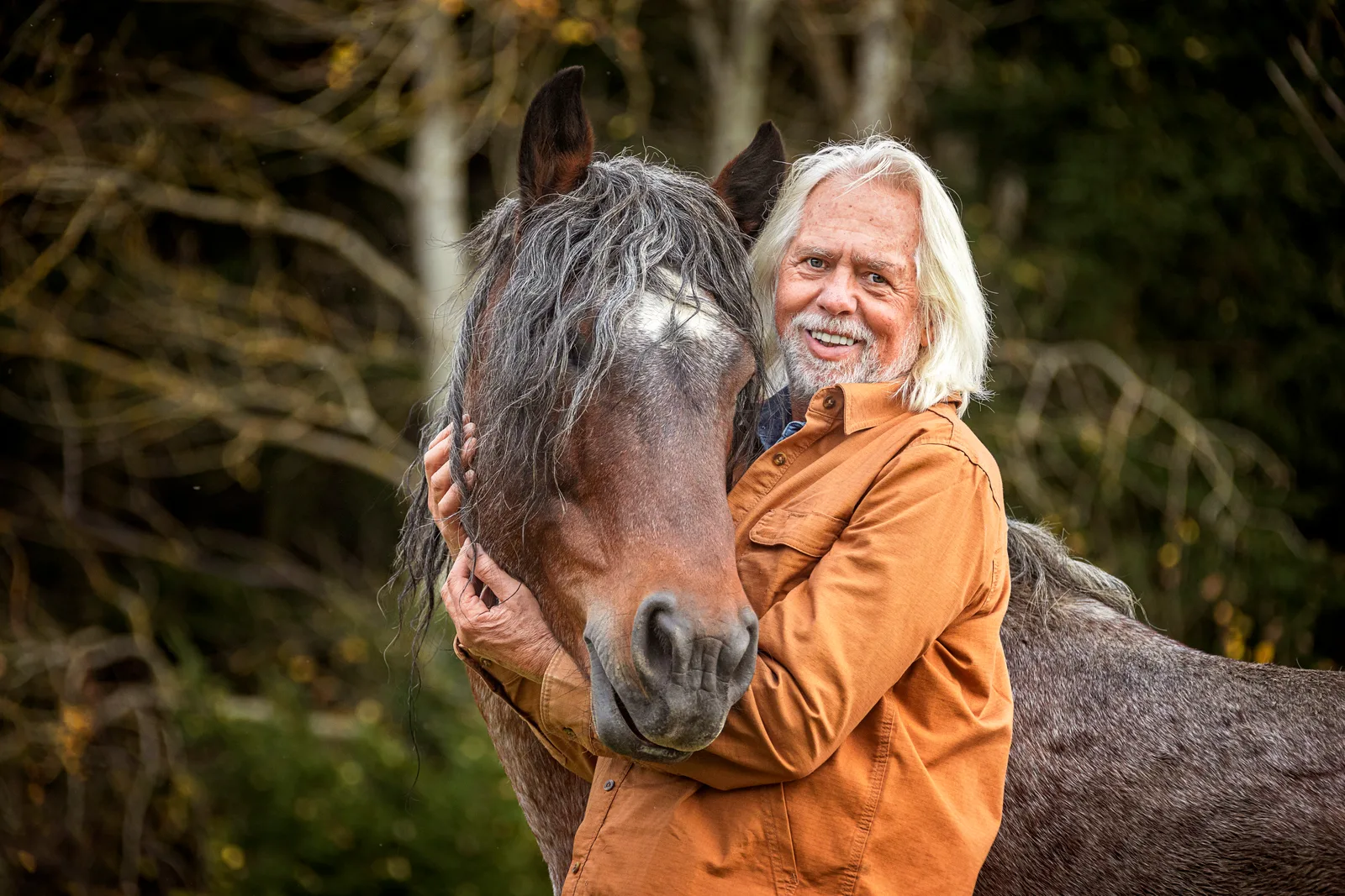 Erich Pröll mit grauem Pferd, orange Jacke, Senior Pferdetrainer