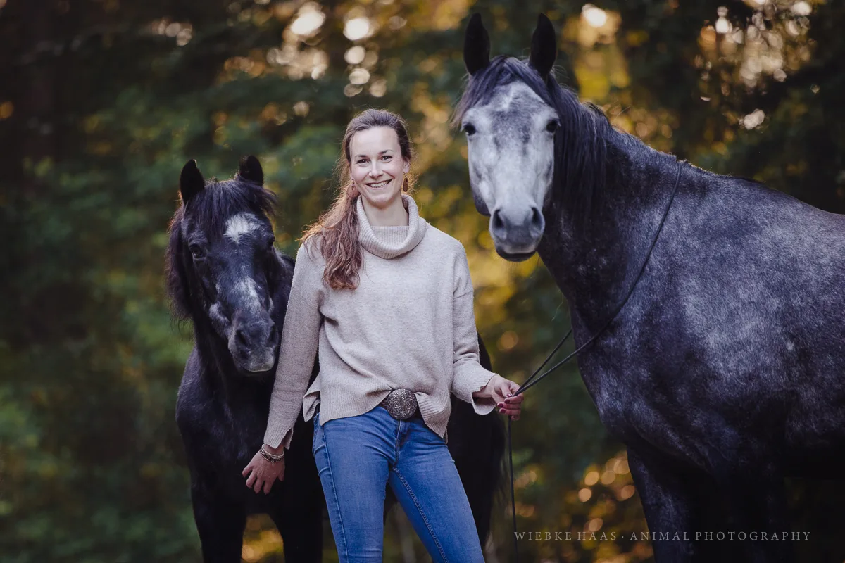 Anna Hochberg mit zwei dunklen Pferden im Herbst, lächelnd zwischen den Tieren