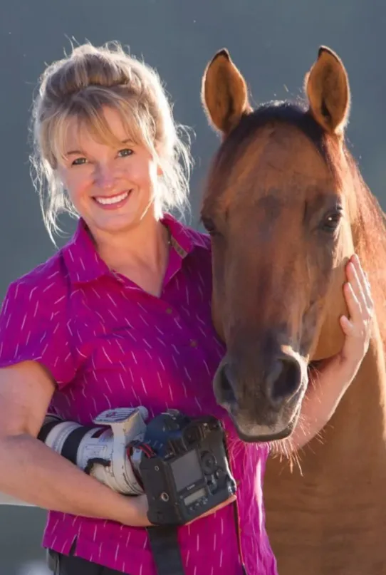 Christiane Slawik mit braunem Pferd, Portraitfoto vor blauem Hintergrund