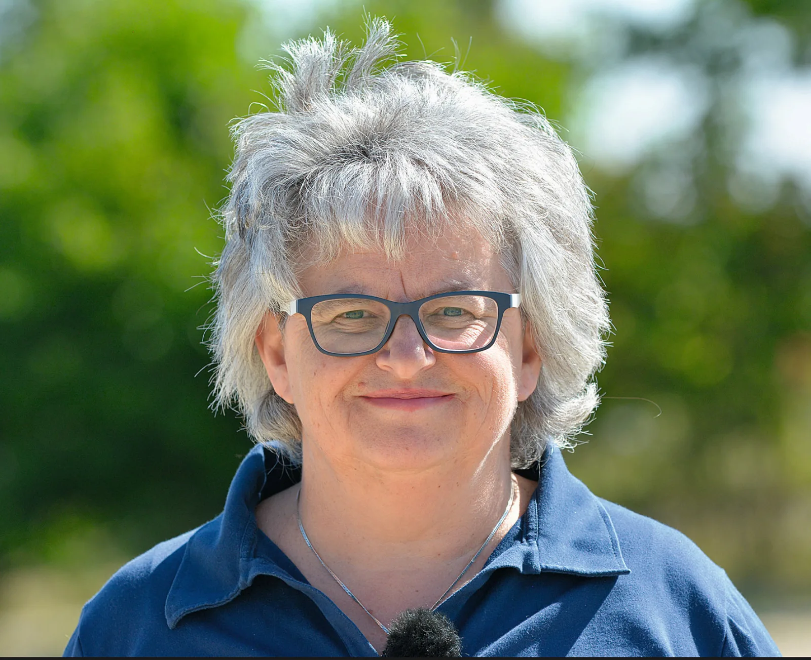 Sibylle Wiemer Porträt, Frau mit grauem Haar und Brille in dunkelblauem Hemd
