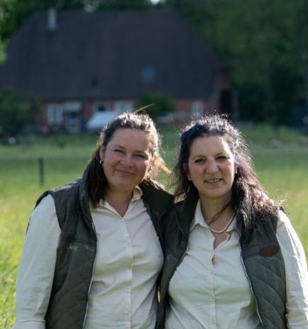Claudia Swierczek und Jennifer Becker, zwei Frauen in weißen Hemden und dunkelgrünen Westen vor Stall