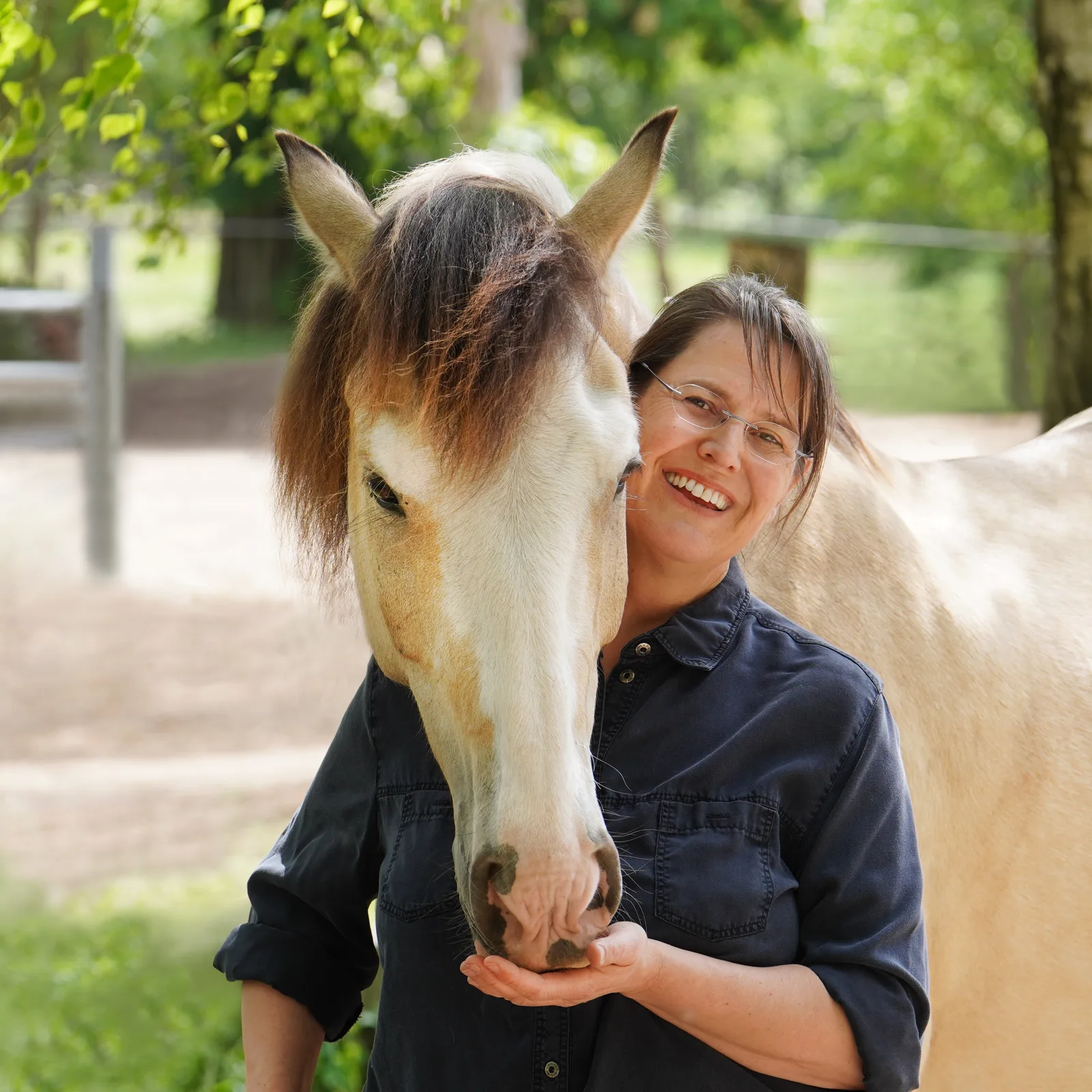 Dr. Christina Fritz lächelnd mit cremefarbenen Pferden im Freien