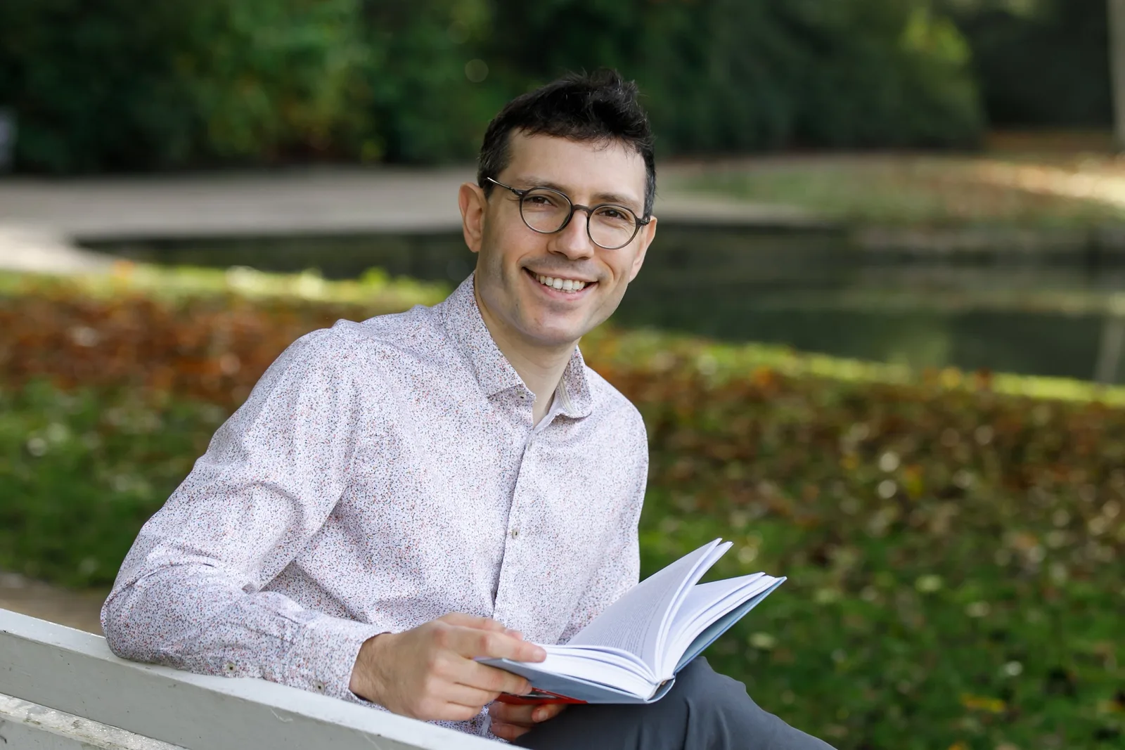 Evgenij Unker sitzt auf Bank mit aufgeschlagenem Buch, grüner Naturhintergrund