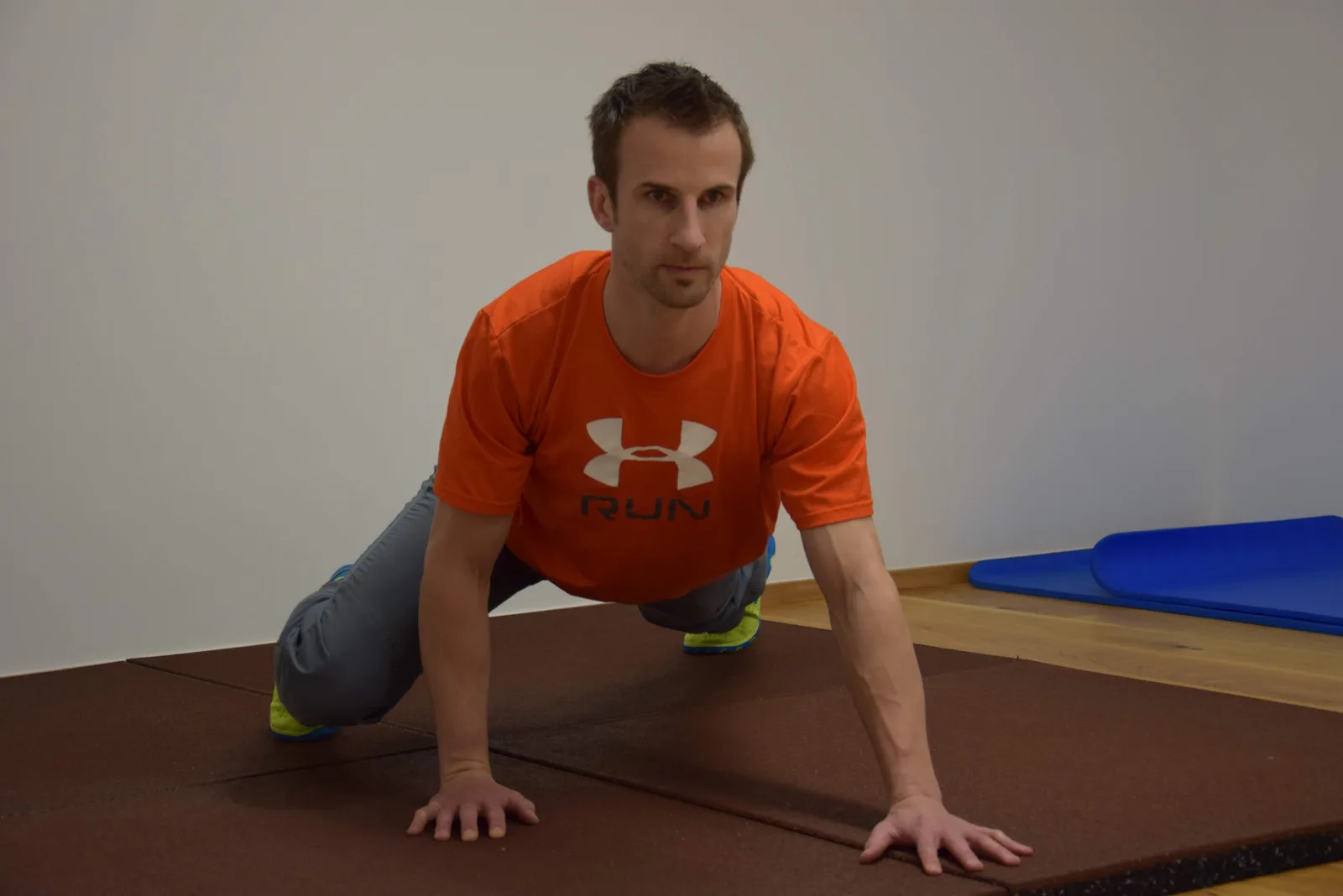 Mann in oranger Under Armour-Shirt in Plank-Position auf Matte, demonstriert Trainingsübung