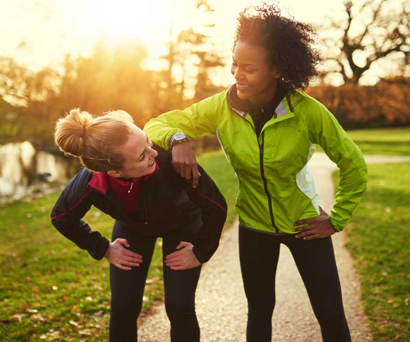 Zwei Läuferinnen in Sportkleidung machen eine Trainingspause im Park beim Sonnenuntergang