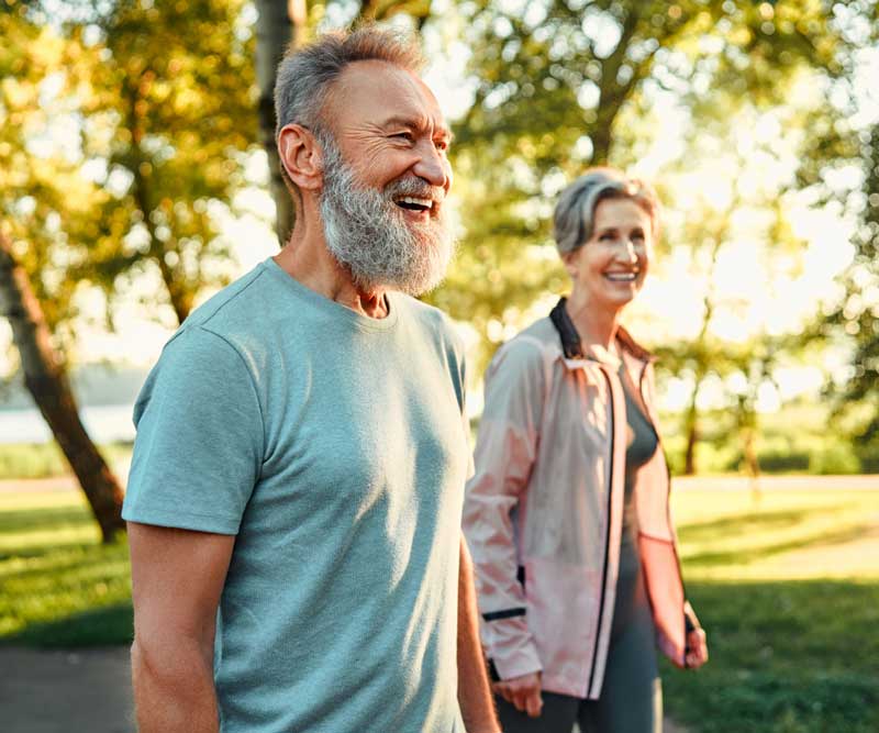 Älterer Mann und Frau laufen gemeinsam im Park, beide lächeln und wirken fit
