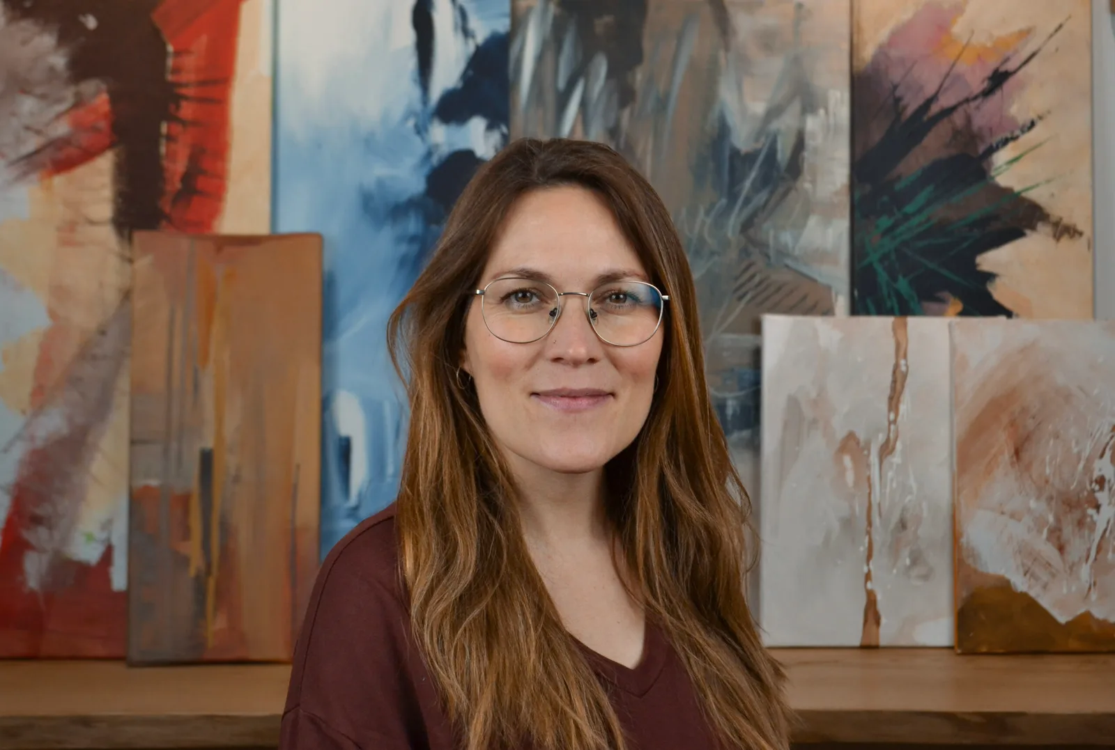 Johanna Menzler Portrait vor bunten abstrakten Kunstwerken, braunes Haar, Brille, Pullover