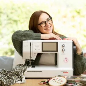 Louise Lemke, Frau mit Brille neben einer Nähmaschine vor grünem Naturhintergrund