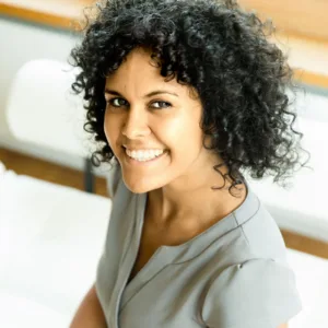 Karima Stockmann, Frau mit lockigen dunklen Haaren in grauem Shirt vor hellem Hintergrund