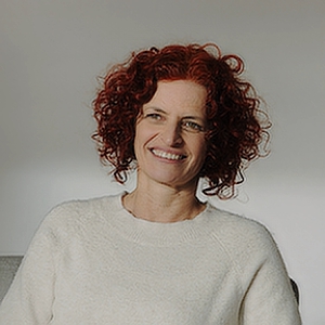 Porträt von Antje Kuwert, Frau mit rotem lockigem Haar, Brille, beigem Oberteil, lächelnd