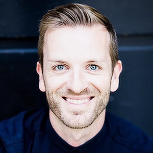 Porträt von Benedikt Zeitner, Mann mit blonden Haaren, blauem Hemd, lächelnd, dunkler Hintergrund