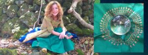 Frau mit rötlichem lockigem Haar in Naturkulisse, sitzt auf moosigem Stein in grünem und blauem Kleid neben kristallinem Obje
