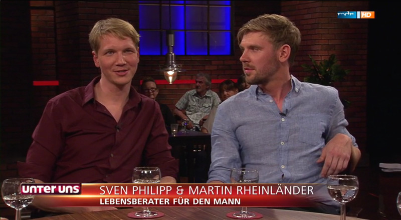 Zwei Männer sitzen sich im Fernsehstudio gegenüber