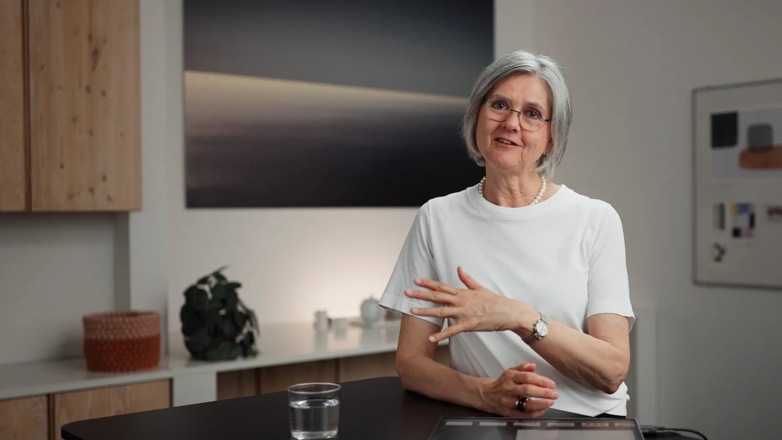 Dr. Antonia Jann in weißem T-Shirt mit Perlenket­te sitzt am Tisch, gestikuliert erklärend, modernes helles Büro im Hintergru