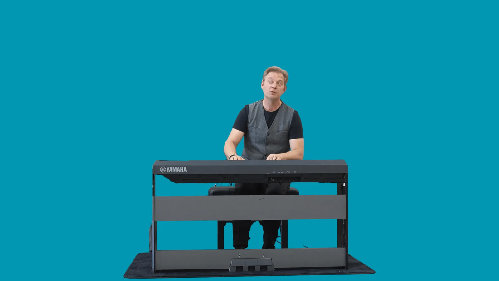 Tilman Lichdi sitzt am Yamaha-Keyboard vor türkisem Hintergrund – Videostandbild