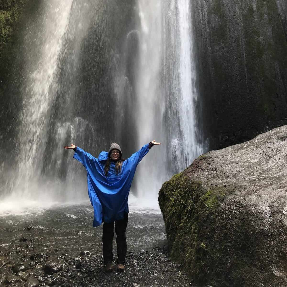 Frau in blauer Jacke mit Armen ausgestreckt vor beeindruckendem Wasserfall