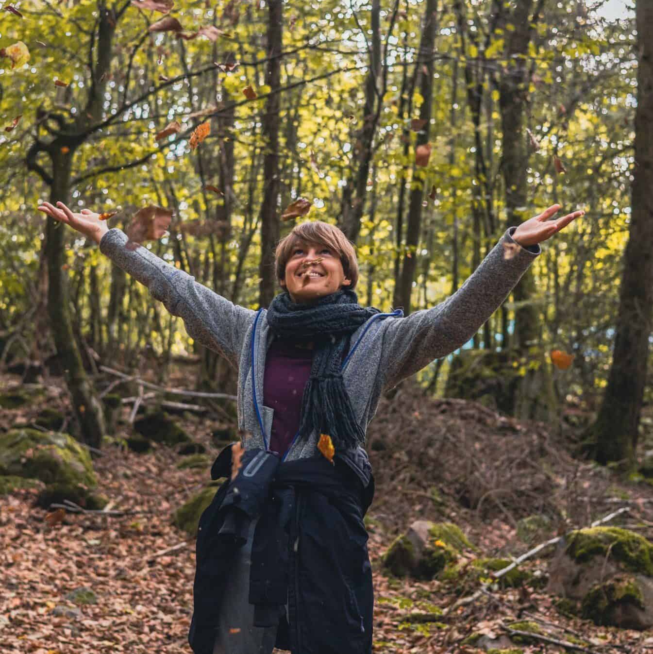 Person mit erhobenen Armen im Herbstwald mit fallenden Blättern, Aktivismus-Geste