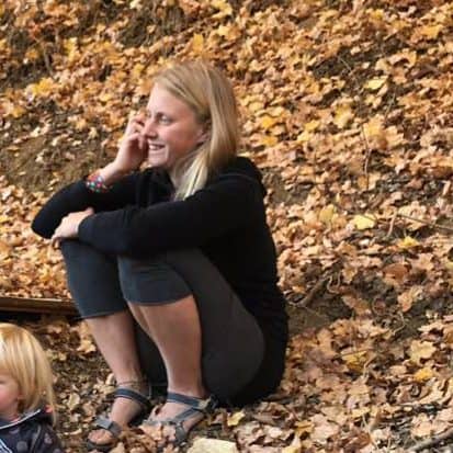 Blonde Frau vor herbstlichem Laubhintergrund in schwarzer Jacke