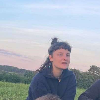 Junge Frau mit Dutt vor grüner Wiese bei Sonnenuntergang