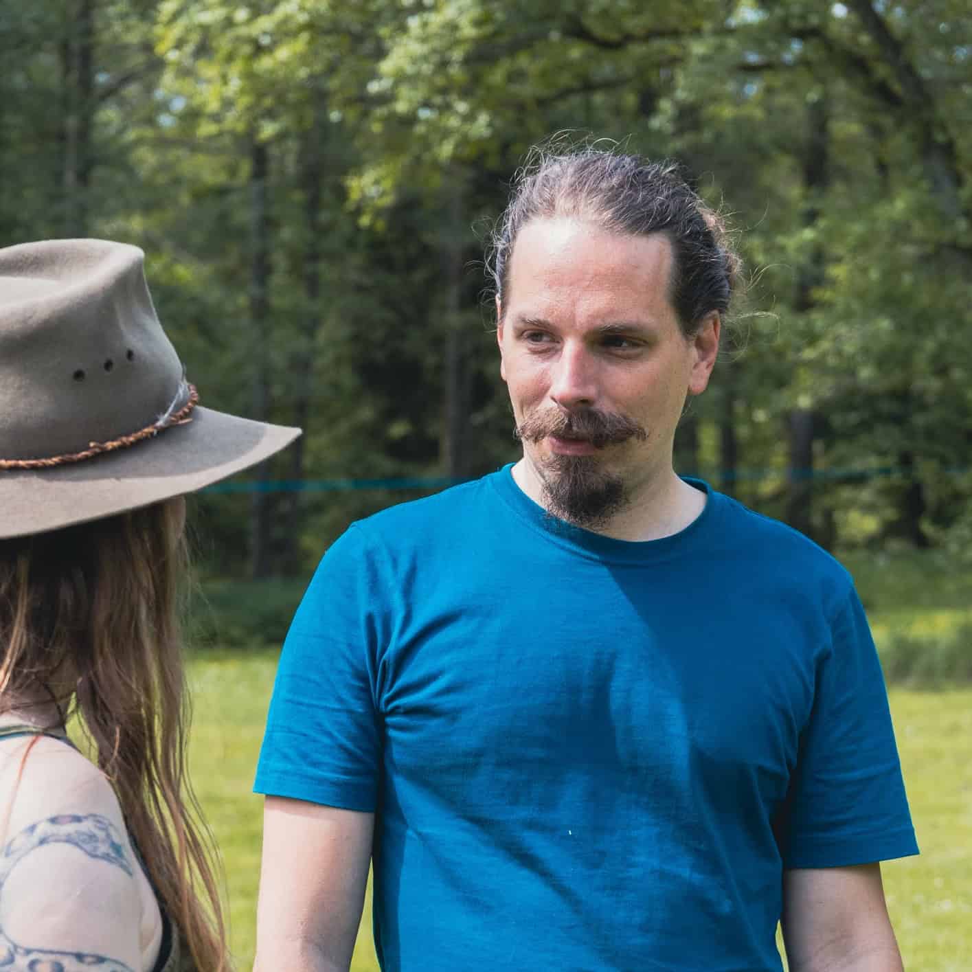 Mann mit Bart in blauem T-Shirt neben Person mit Cowboyhut