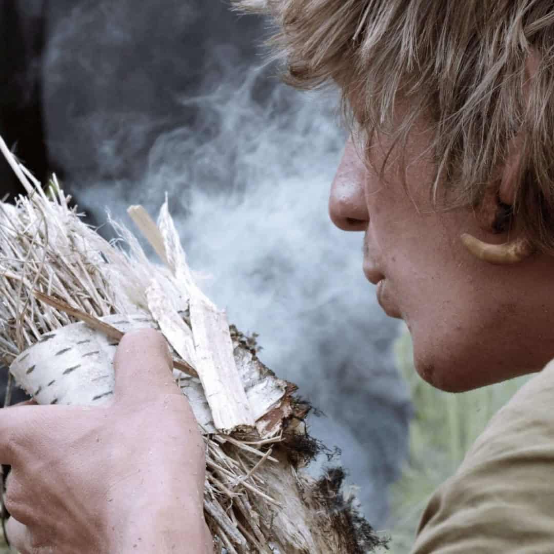Porträt eines jungen Mannes mit braunen Haaren, der ein Stück Birkenrinde hält und konzentriert nach unten schaut