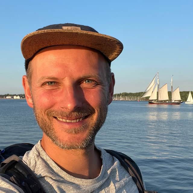 Porträt eines bärtigen Mannes mit Hut vor Segelbooten auf dem Wasser