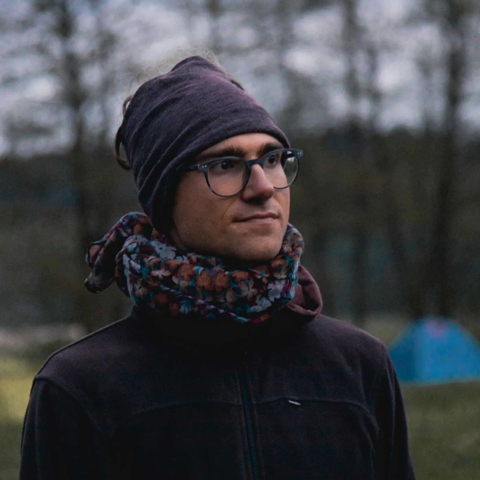 Person mit Brille, Beanie und Schal vor unscharfem Waldwald